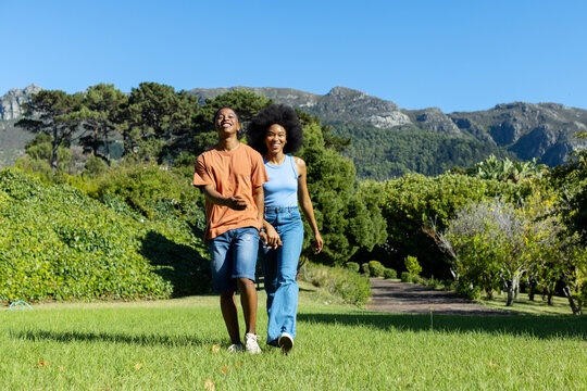African American couple holding hands walking across lawn in park wearing denim and sneakers