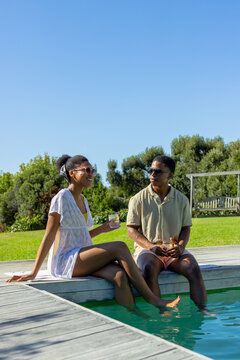 African American couple sitting on wooden deck, feet in water, woman wearing lace coverup, shades