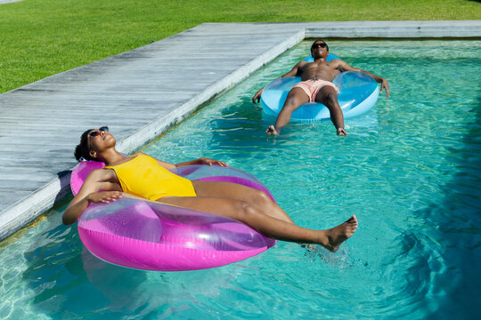 African American couple lounging on floats at backyard pool with yellow swimsuit and shades