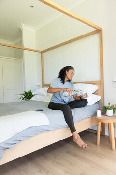 Adult woman of African descent sitting on four-poster bed pouring water, wearing light blue T-shirt