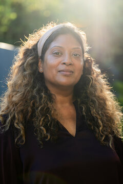Vertical video: Facing woman holding calm look in park as sun backlit creating flare, with headband