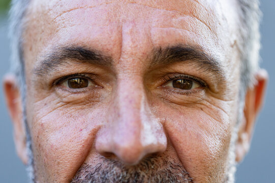 Senior man holding steady gaze, revealing textured skin and catching light on brown eyes in studio