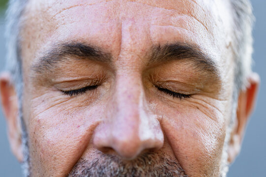Senior male showing closed eyes in studio close-up, highlighting skin texture and stubble