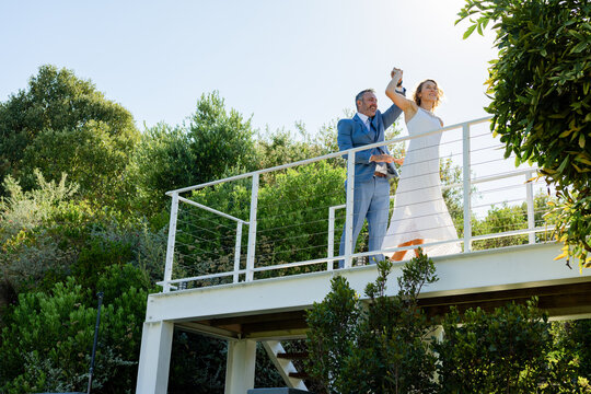 African American couple by cable railing on deck, man lifting bride's hand for photos, copy space
