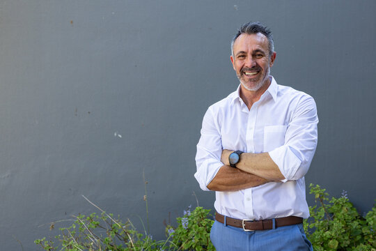 Man standing on right by concrete wall wearing white shirt, blue trousers, belt, watch, copy space