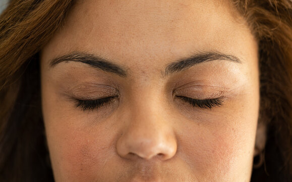 Woman resting with closed eyes in studio, showing eyelashes, small hoop earring, skin texture