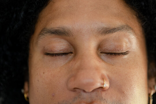 African American adult male having eyes shut in closeup showing gold nose hoop, earrings, stubble