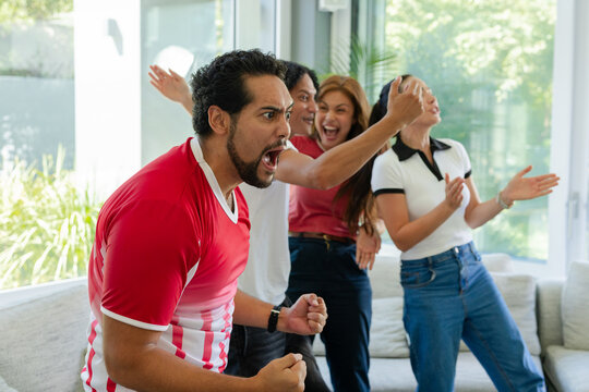 African American friends, man in red jersey, cheering on sofa by large glass windows, copy space