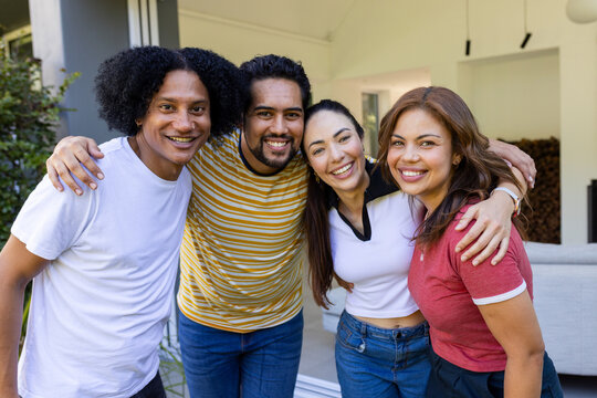 Diverse friends wearing casual clothing smiling and leaning on covered patio at home, sofa inside