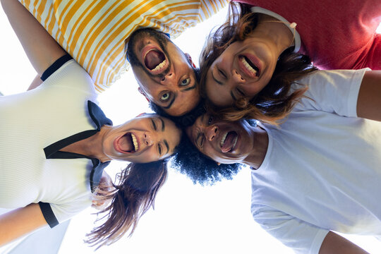 Diverse friends leaning in laughing and shouting outside under bright sky wearing striped shirt