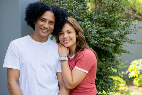 African American couple smiling and leaning in garden showing smartwatch white tee and red ringer