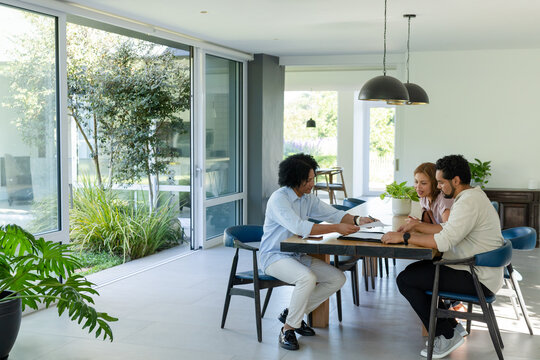 Three African American adults sitting at dining table reviewing documents with pen by glass doors