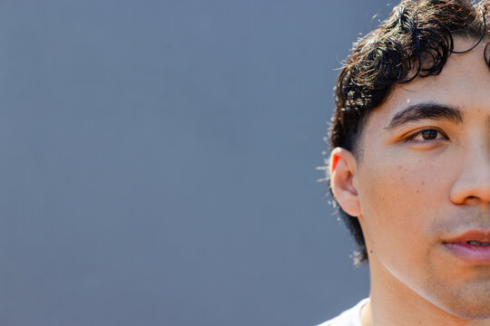 Asian man looking slightly off camera against blue gray wall wearing white T-shirt, copy space