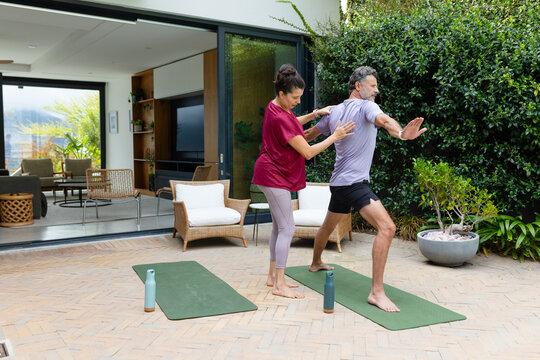 Exercise pair doing yoga on mats with water bottles near glass door, woman adjusting man's posture
