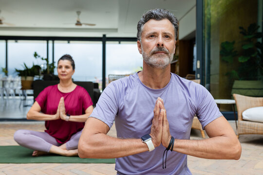 Couple meditating on tiled patio on green mats, man wearing light purple shirt and smartwatch