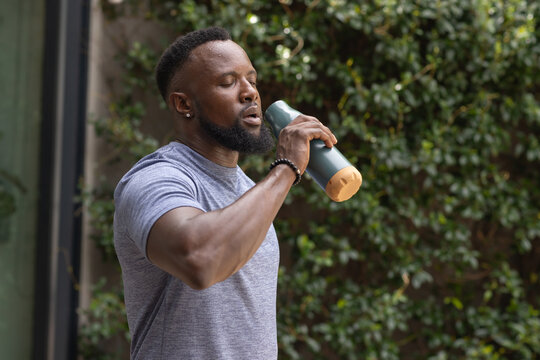 African American man pausing at doorway drinking from green water bottle wearing fitted grey tee