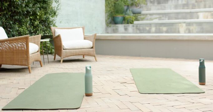 Camera panning upward revealing two olive yoga mats with turquoise bottles on brick patio for yoga