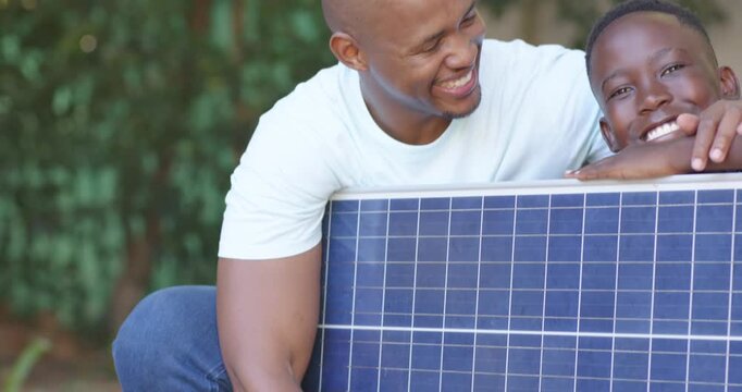 African American father and son steadying solar panel to install, son resting chin and both smiling