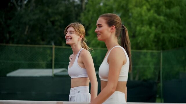 Female tennis players smiling and shaking hands at court net after friendly game. Outdoor tennis moment with positive emotions.