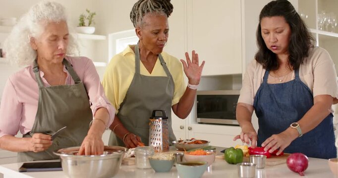 Diverse female friends wearing aprons starting prep at kitchen island, chopping peppers, grating