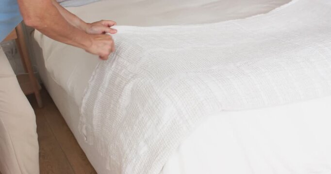 Diverse couple starting day, smoothing and tucking white bedspread in bedroom while man inspecting