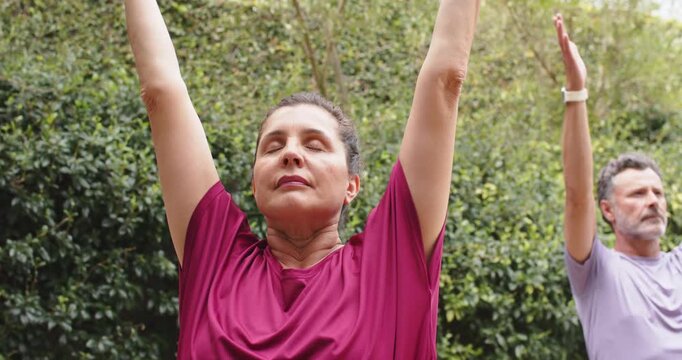 Senior couple breathing, woman lifting arms overhead in garden for yoga with watch and lapel mic