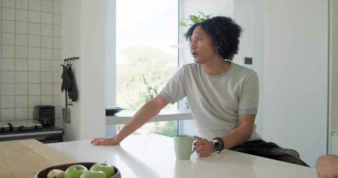Men sitting at kitchen island, reacting to woman speaking while holding green mugs, phone appearing