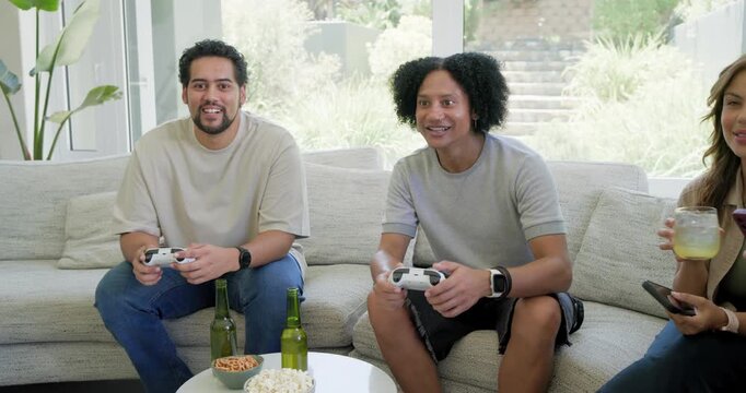 Friends on light couch watching two men gripping white controllers and reacting to decisive play