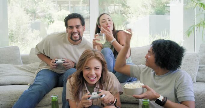 Diverse friends playing game on couch holding controllers popcorn cheering after win then chatting