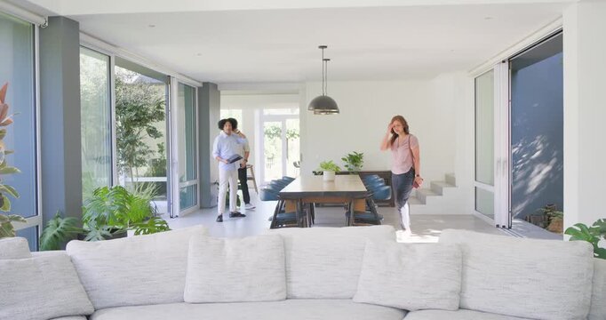 Two men and one woman entering through doorway, touring home, host holding folder pointing at sofa