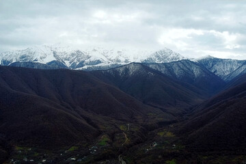 Fototapeta premium Aerial View of Snow-Capped Mountain Range Over Small Rural Village. A scenic landscape showing towering, snow-covered peaks overlooking a valley with a small town and a dry riverbed