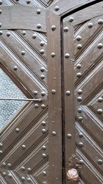 Slow smooth pan from left to right across a beautifully carved antique wooden door with intricate geometric diamond patterns and decorative metal studs. Classic European medieval architecture detail i