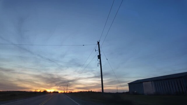 Driving Past a Farmhouse at Sunset With Colorful Skies