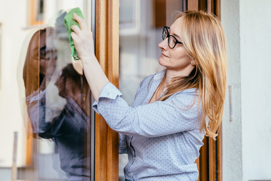 Middle aged caucasian woman cleaning window glass with cloth at home