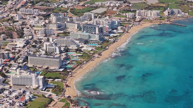 Aerial drone view of modern beachfront hotels along the coast of Protaras, Cyprus, with golden sand beaches and clear blue water attracting tourists to this Mediterranean destination