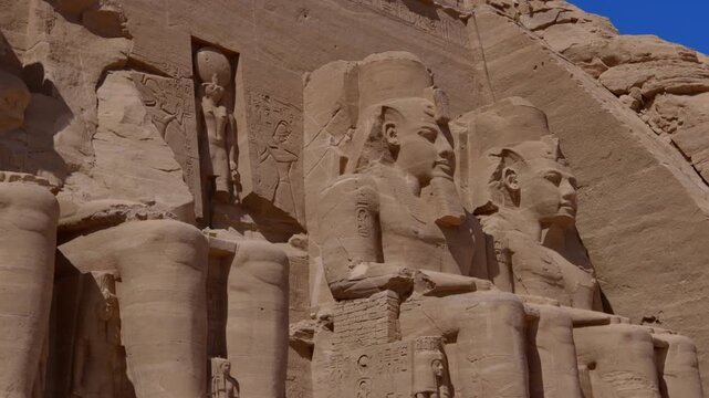 Close-up of giant Ramesses II colossi carved into rock facade at Abu Simbel temple, Egypt. Dramatic upward view of ancient sandstone pharaoh statues. Travel and history.