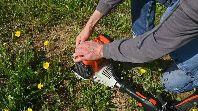 Hands of an Active Senior Man Starting Brush Cutter with Pull Cord, Outdoor Landscaping Work and Rural Lifestyle Concep