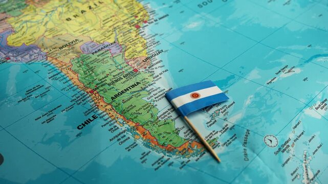 Hand pushes small Argentina flag on geographic map