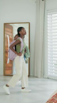 Vertical video: Opening wooden door, mom leading daughters home, carrying backpacks and mesh bag