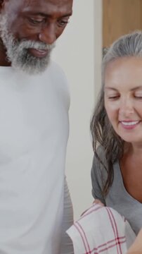 Vertical video: Camera framing couple lifting tea towel, turning pan, checking base in kitchen