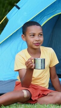 Vertical video: Sitting youth holding mug at blue tent with knee bandage yellow shirt orange shorts