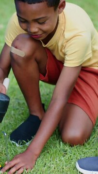 Vertical video: Kneeling youth tapping metal peg on lawn after helper handing dowel to secure peg