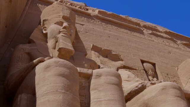 Close-up of giant Ramesses II colossi carved into rock facade at Abu Simbel temple, Egypt. Dramatic upward view of ancient sandstone pharaoh statues. Travel and history.