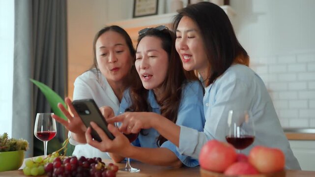 Three Asian women friends taking group selfie in kitchen, holding wine glasses, smiling and laughing, joyful reunion sharing old memories, bonding, good vibes and warm home lifestyle moment together.