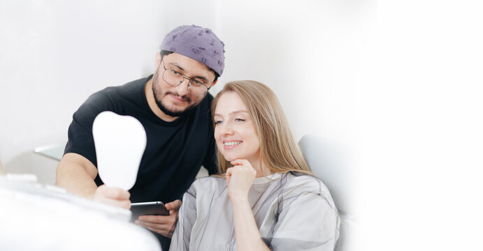 Young caucasian female smiling with hispanic male dentist with tablet computer holding mirror in dental office, consultation in stomatology clinic white banner
