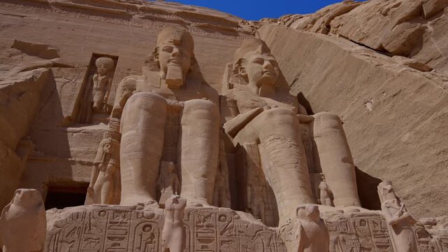 Close-up of giant Ramesses II colossi carved into rock facade at Abu Simbel temple, Egypt. Dramatic upward view of ancient sandstone pharaoh statues. Travel and history.
