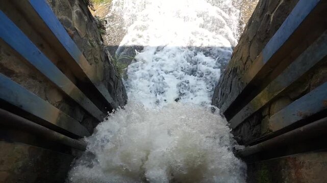 the flow of river water that passes over a small dam or threshold, creating a waterfall effect with white foam that contrasts with the brownish color of the river water
