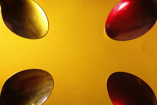 Cucharas de metal para sopas y postres, coloreadas con luz vertical de color rojas y amarillas ordenadas en las esquinas de la fotograf&iacute;a, presenta un original dise&ntilde;o abstracto con fondo amarillo.
