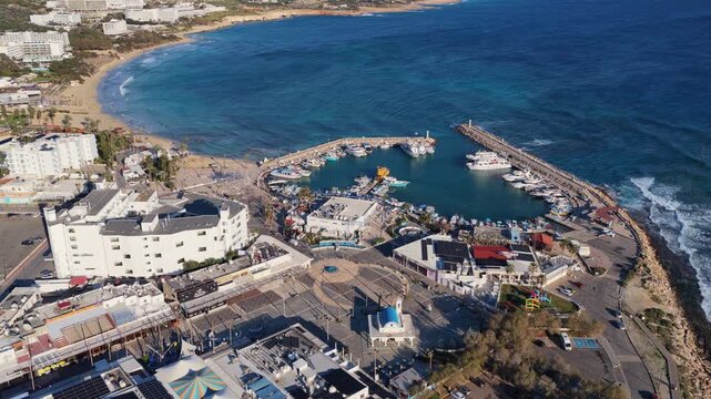 Aerial drone view of a small marina and harbor with boats docked and curved breakwaters protecting the coastline, Ayia Napa, Cyprus