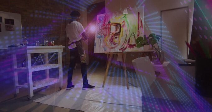 Artist lifting brush and holding lamp, painting strokes to refine composition under patterned light